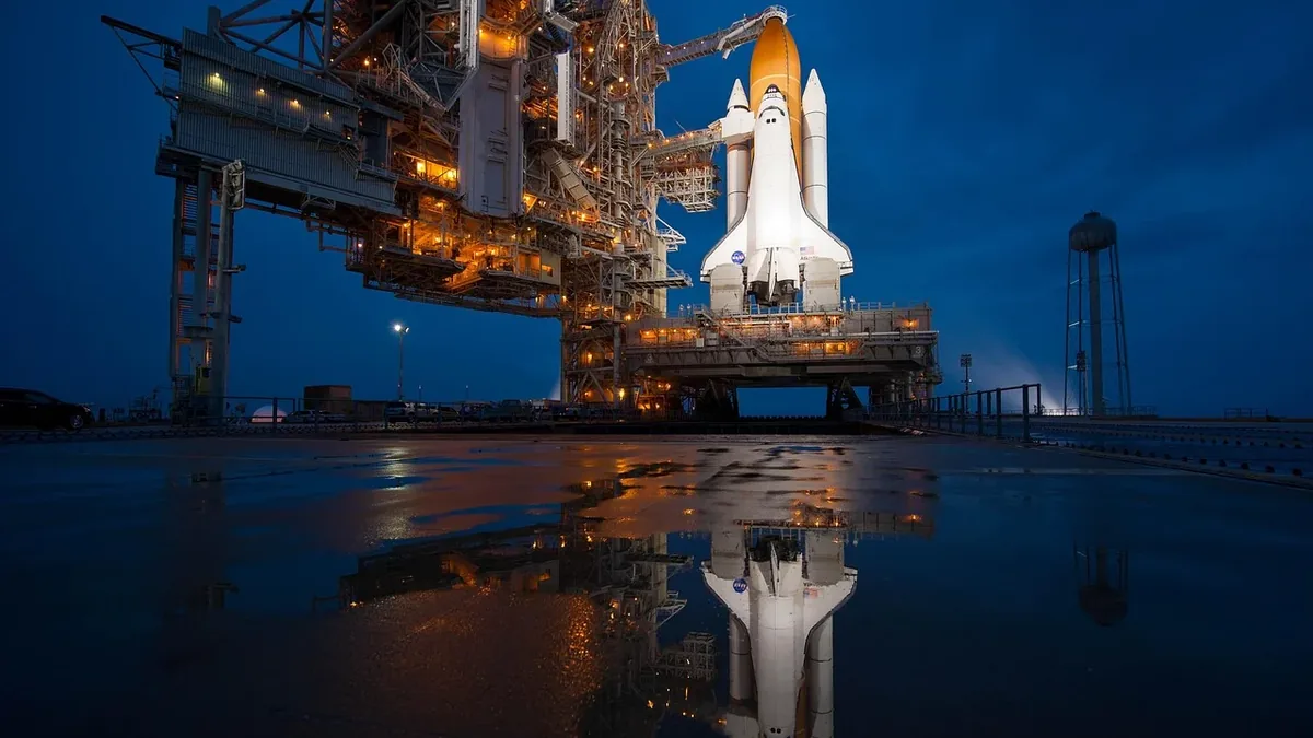 The Space Shuttle Discovery on the launch pad at Kennedy Space Center, with the shuttle's white body and orange flame visible.