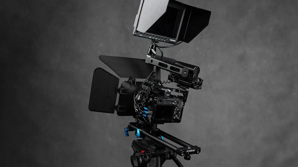 A professional video camera mounted on a tripod, with a monitor attached to the top.