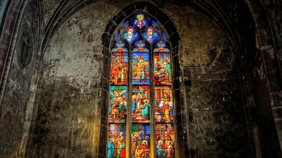 A stained glass window with a religious scene, set within an arched stone wall.