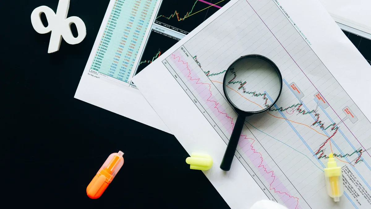 A magnifying glass, a percentage sign, and various graphs and charts on a black surface.